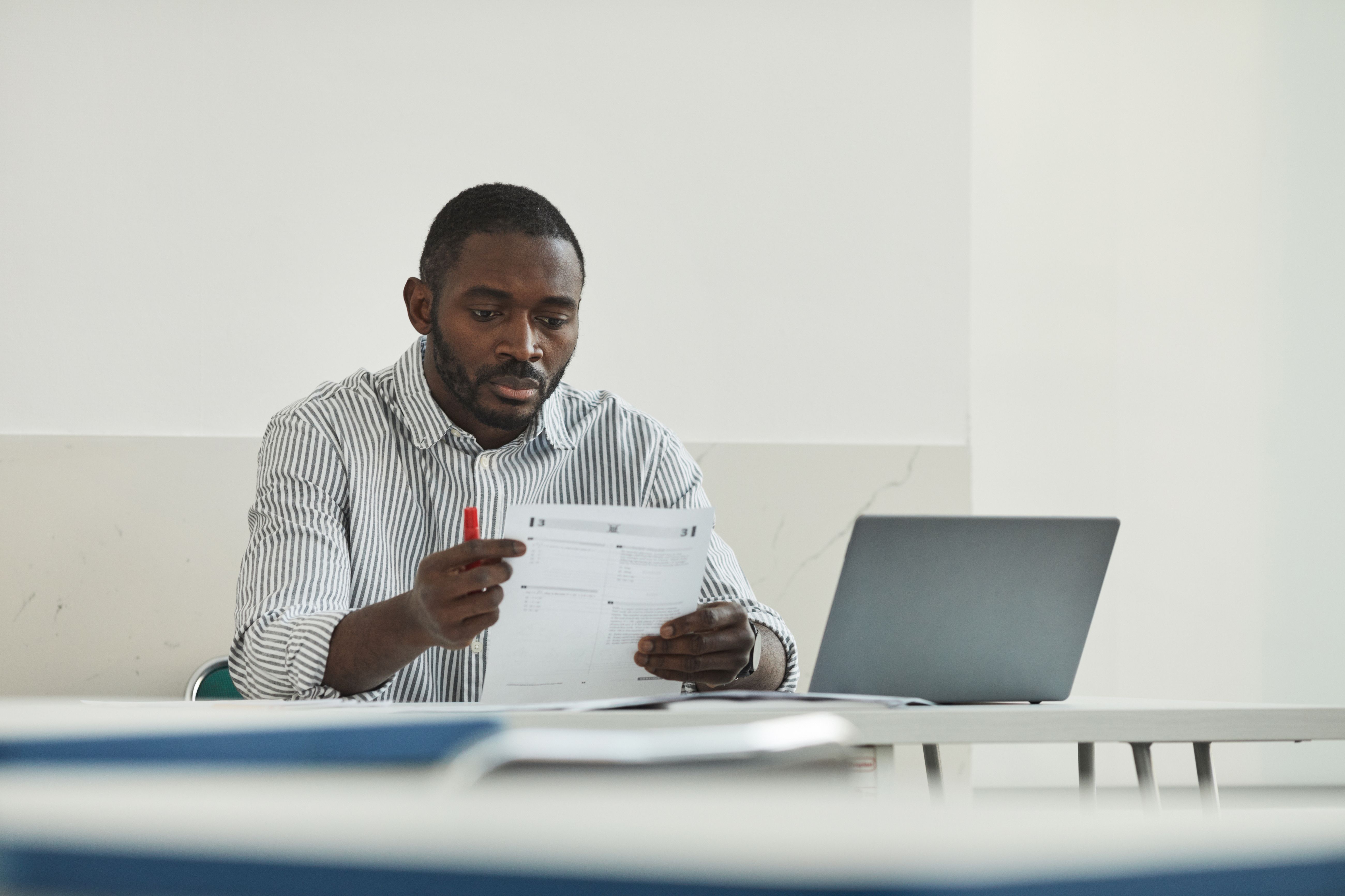 Professional at a desk carefully reviewing a printed document beside a laptop